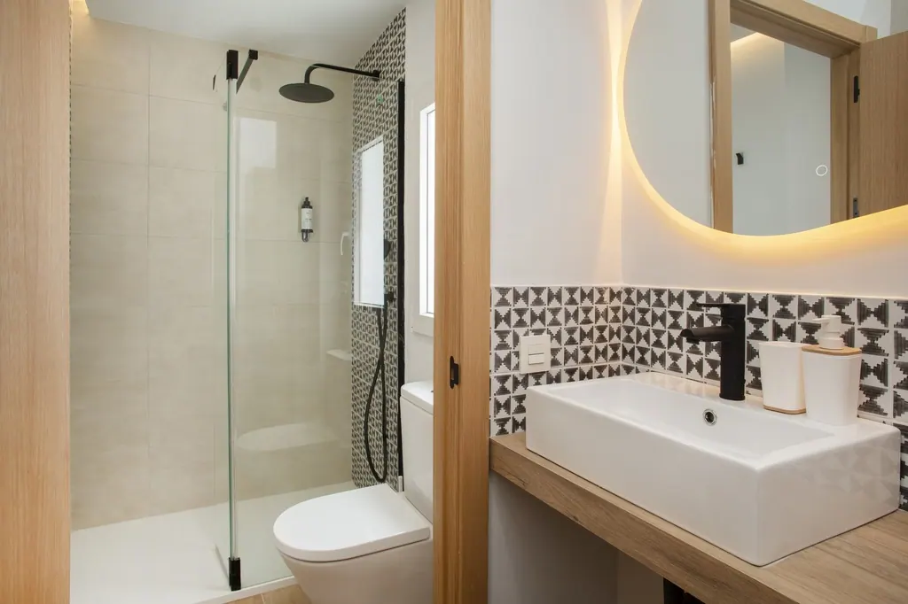 Holiday Home for Rent Baño moderno con azulejos geométricos, espejo redondo iluminado y ducha de cristal