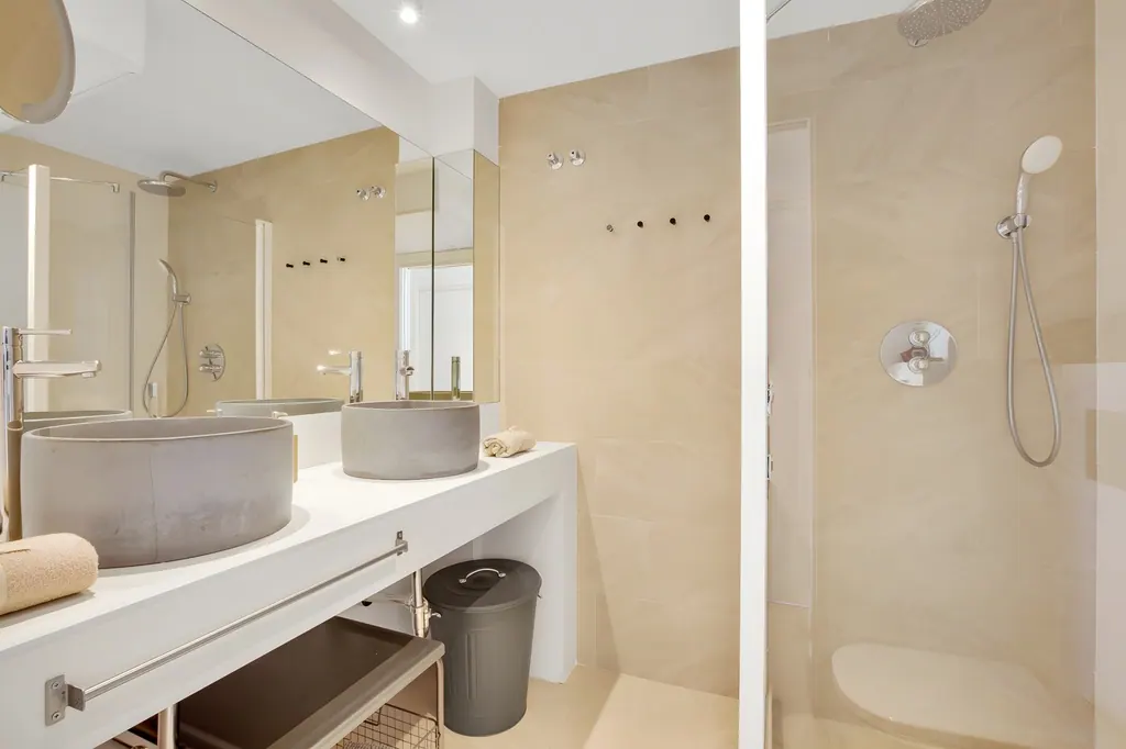 Penthouse la Carihuela Baño moderno con lavabos de hormigón, ducha y acabados beige minimalistas